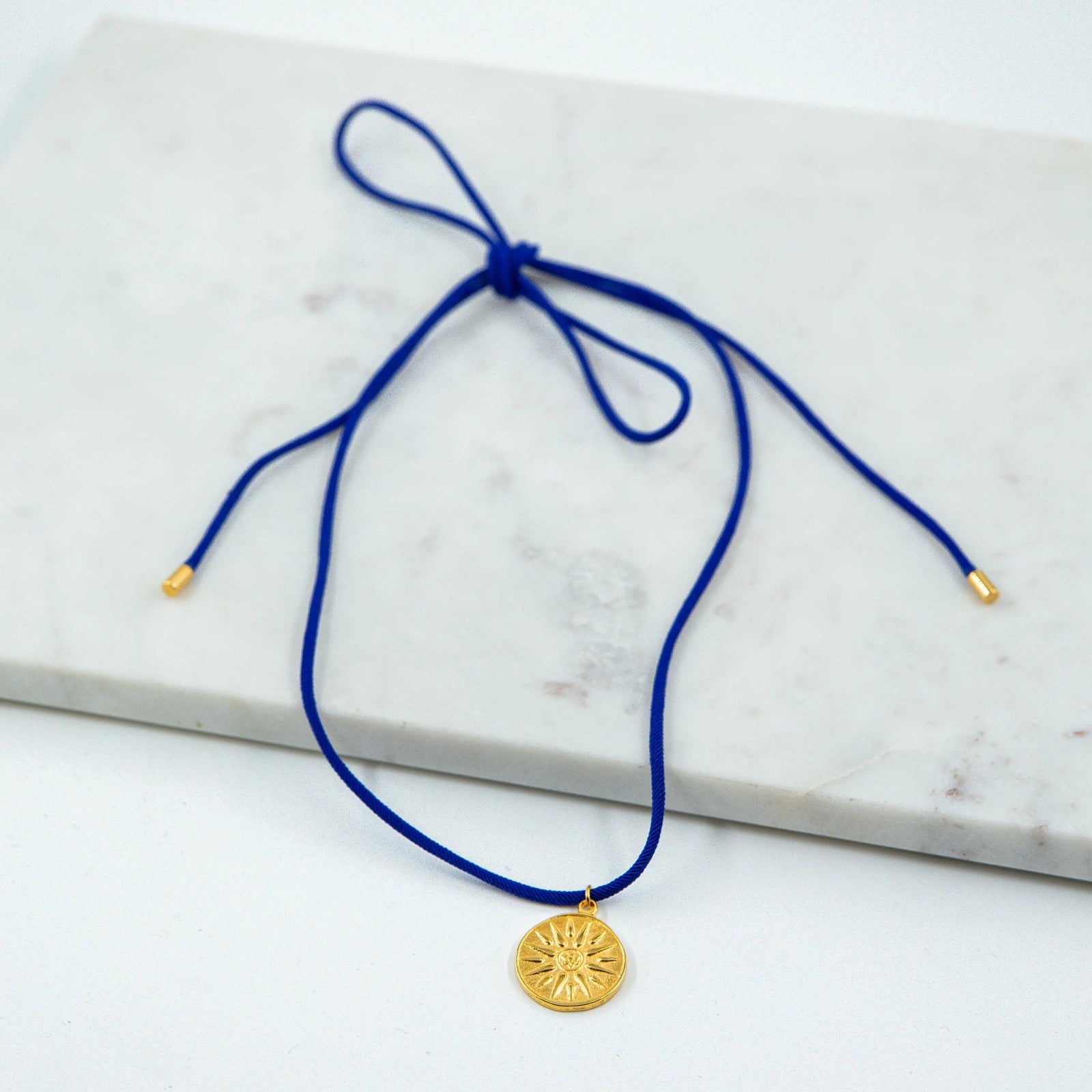 Collier Soleil de Vergina - Symbole Royal et Élégance Artisanale  Plongez dans l'héritage fascinant de l'Antiquité avec notre Collier Soleil de Vergina, une pièce unique faite à la main par nos artisans avec une passion pour l'art et l'histoire. Ce collier est orné d'une pièce antique représentant le célèbre Soleil de Vergina, découvert dans une tombe royale macédonienne attribuée à Philippe II, le père d'Alexandre le Grand.